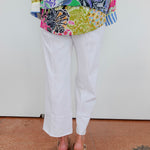Person wearing a colorful patterned top and white pants on a plain background