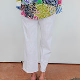 Person wearing a colorful patterned top and white pants on a plain background