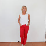 Woman wearing a white sleeveless top and red pants standing against a white wall.