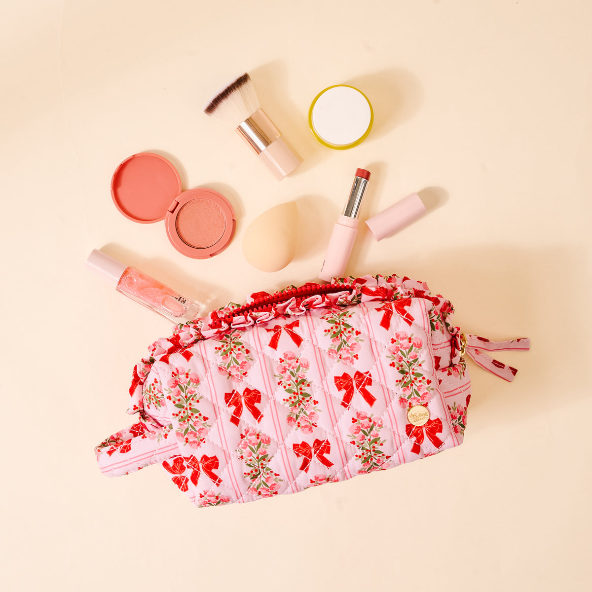 Makeup bag with floral and bow design surrounded by makeup items on a beige background