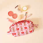 Makeup bag with floral and bow design surrounded by makeup items on a beige background