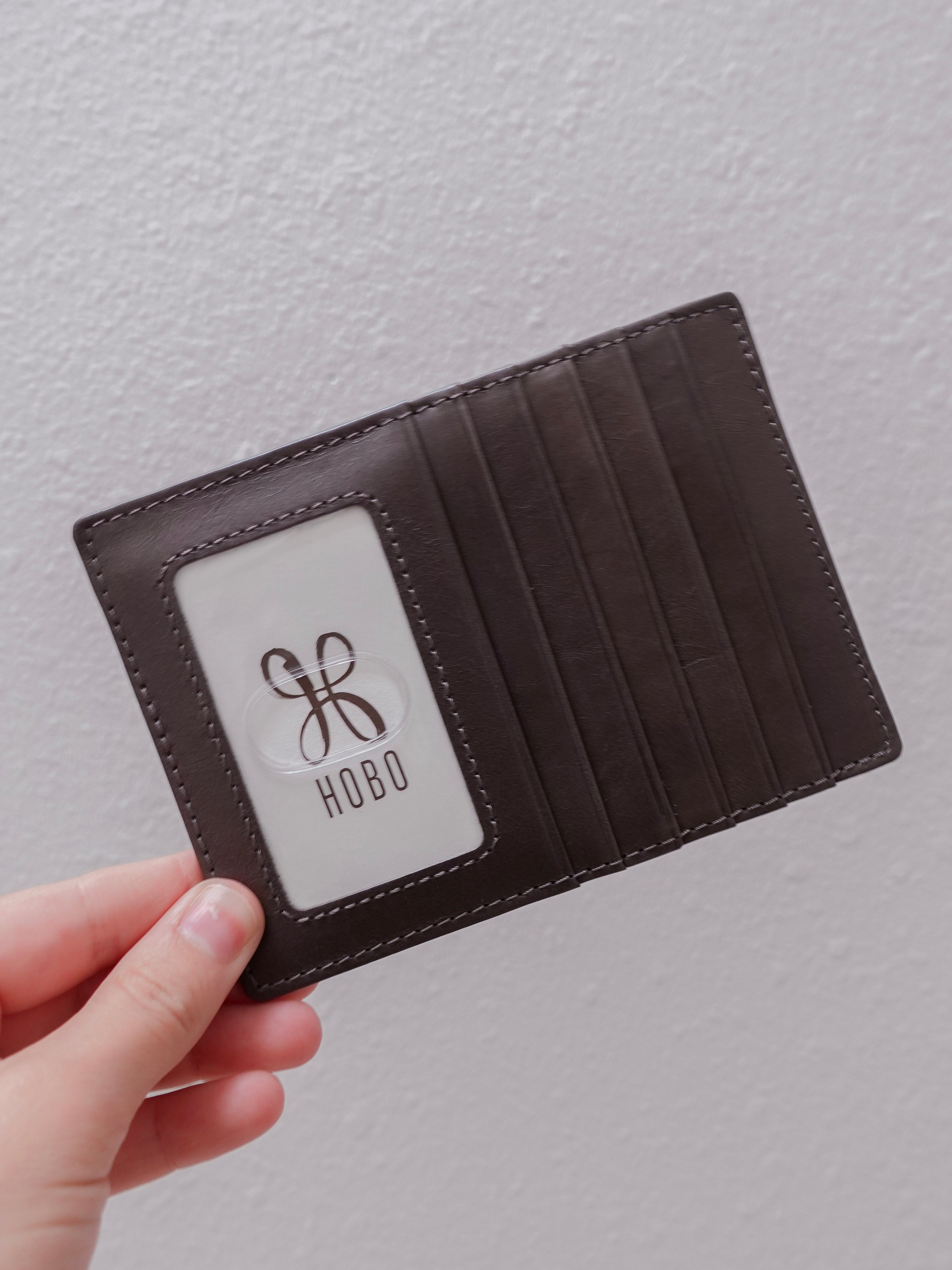 Brown leather wallet held by a hand with 'Hobo' logo on a light gray background