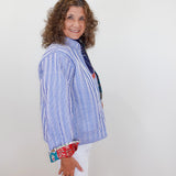 Woman wearing a blue and white striped shirt with a colorful pattern on the cuffs against a white background