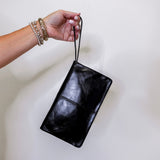 Black leather clutch held by a hand against a white background
