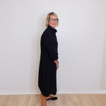 Person wearing a black dress standing against a white wall.