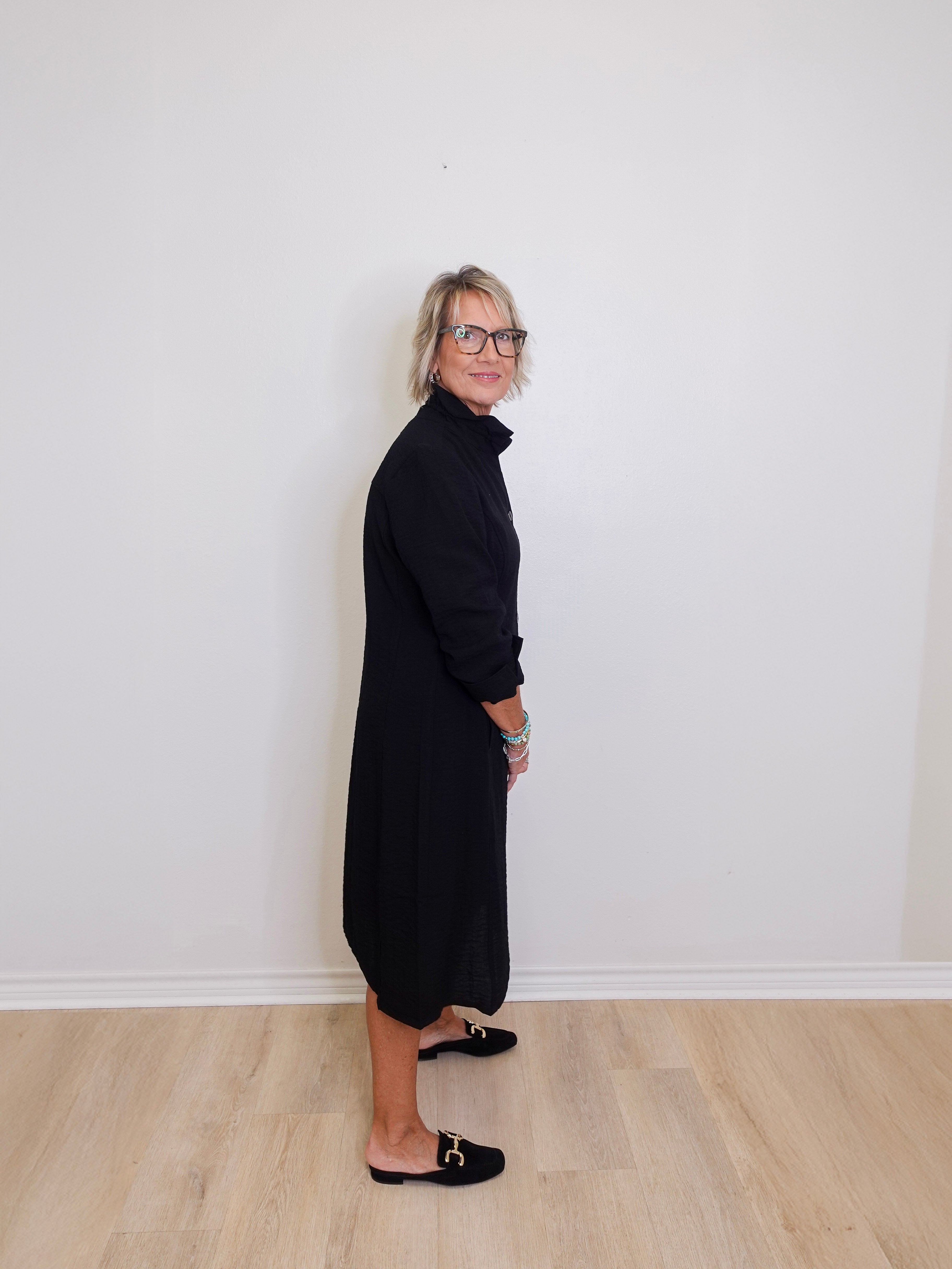 Person wearing a black dress standing against a white wall.