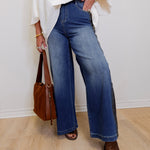 Person wearing blue jeans and a white top, holding a brown bag indoors.