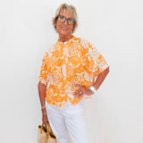Woman wearing an orange floral blouse and white pants against a white background