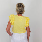 Person wearing a yellow top with ruffled sleeves and a white skirt against a plain background