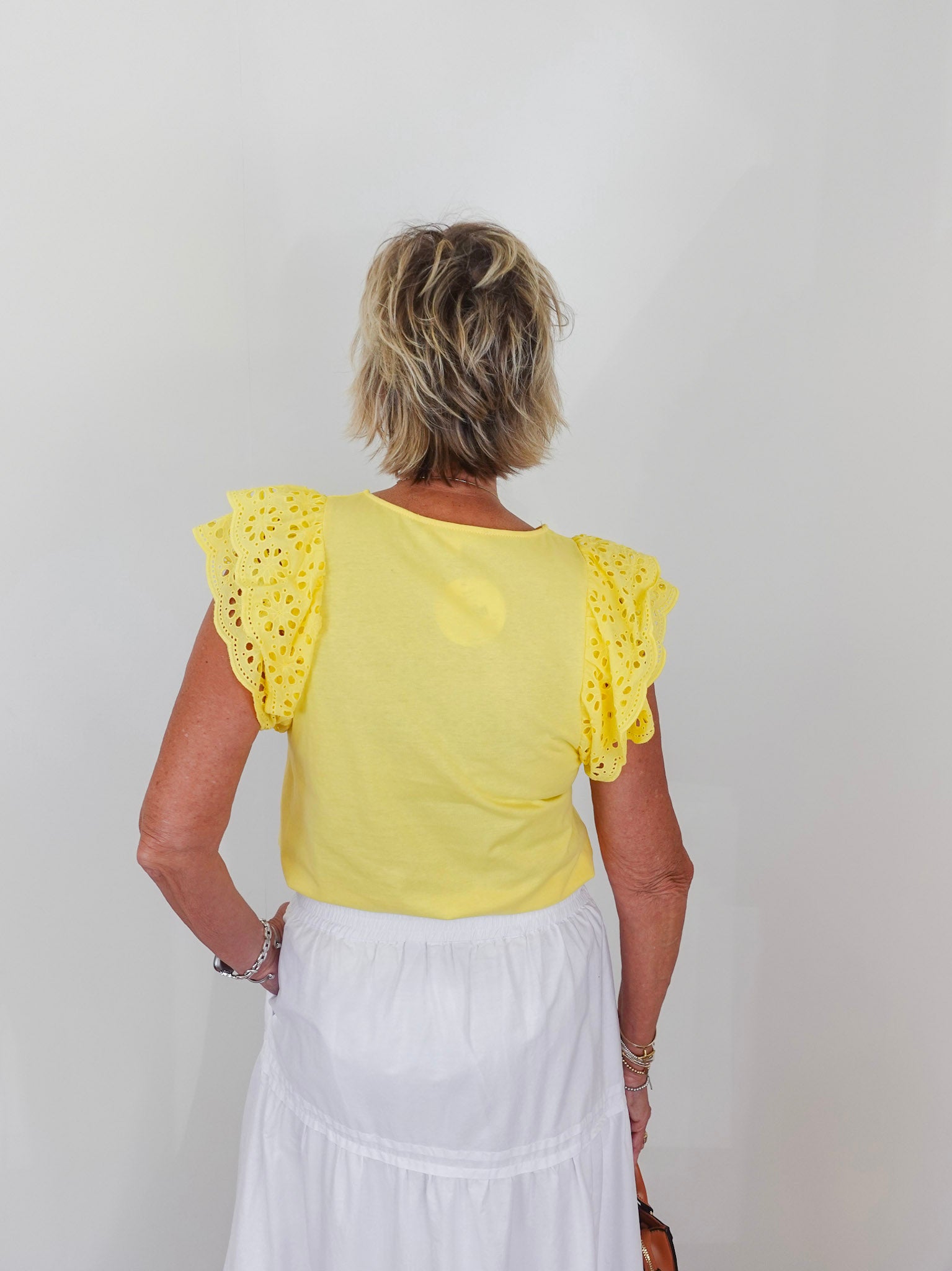 Person wearing a yellow top with ruffled sleeves and a white skirt against a plain background