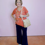 Woman wearing a red floral shirt, dark blue pants, and white shoes against a pink wall.