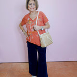 Woman wearing a red floral shirt, dark blue pants, and white shoes against a pink wall.