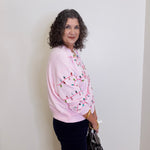 Woman wearing a pink sweater with a pattern, standing against a white wall.
