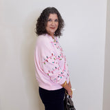 Woman wearing a pink sweater with a pattern, standing against a white wall.