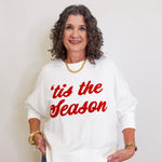 Woman wearing a white sweatshirt with 'tis the season text in red on a plain background