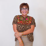 Woman wearing a leopard print top with colorful embroidery against a white background