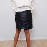 Person wearing a black leather skirt and white sweater against a plain background
