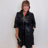Woman wearing a black leather dress against a white wall