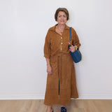 Woman wearing a brown top and skirt with a blue bag against a white wall.