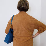 Person wearing a brown jacket with a blue bag against a white wall