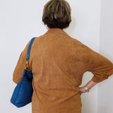 Person wearing a brown jacket with a blue bag against a white wall