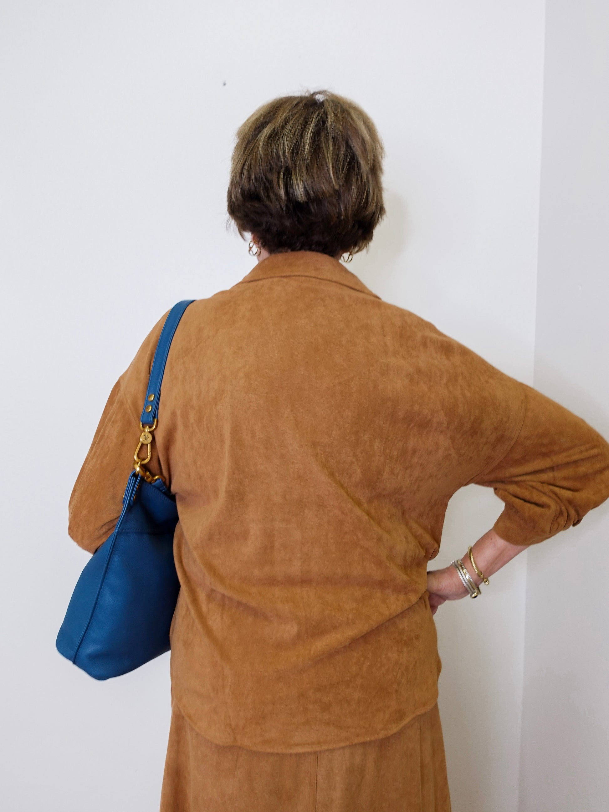 Person wearing a brown jacket with a blue bag against a white wall
