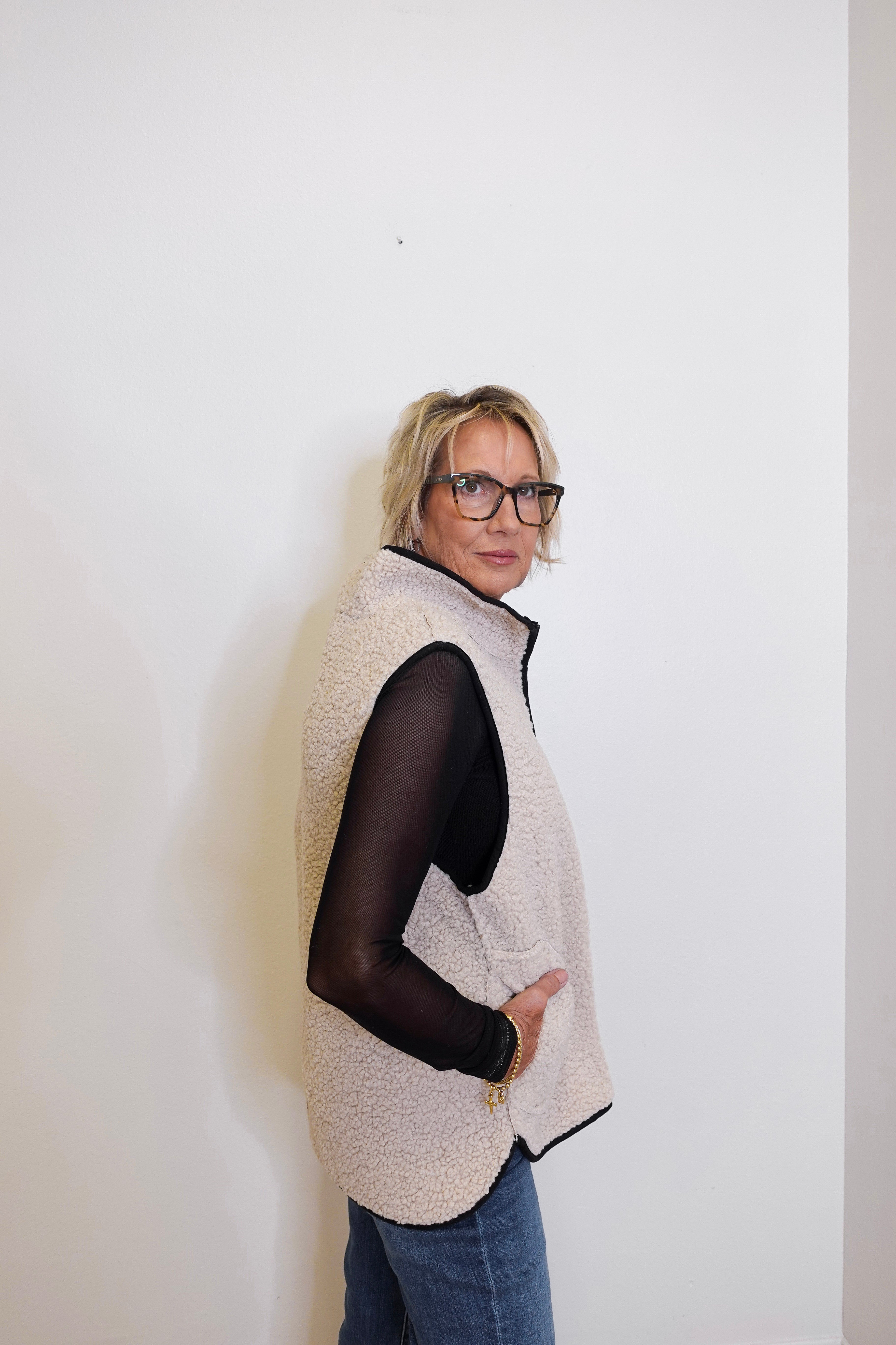 Person wearing a beige vest over a black top against a white background