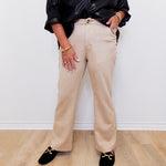 Person wearing a black leather jacket, beige pants, and black loafers on a light wooden floor.