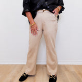 Person wearing a black leather jacket, beige pants, and black loafers on a light wooden floor.