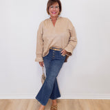 Woman wearing a beige sweater and blue jeans standing against a white wall.