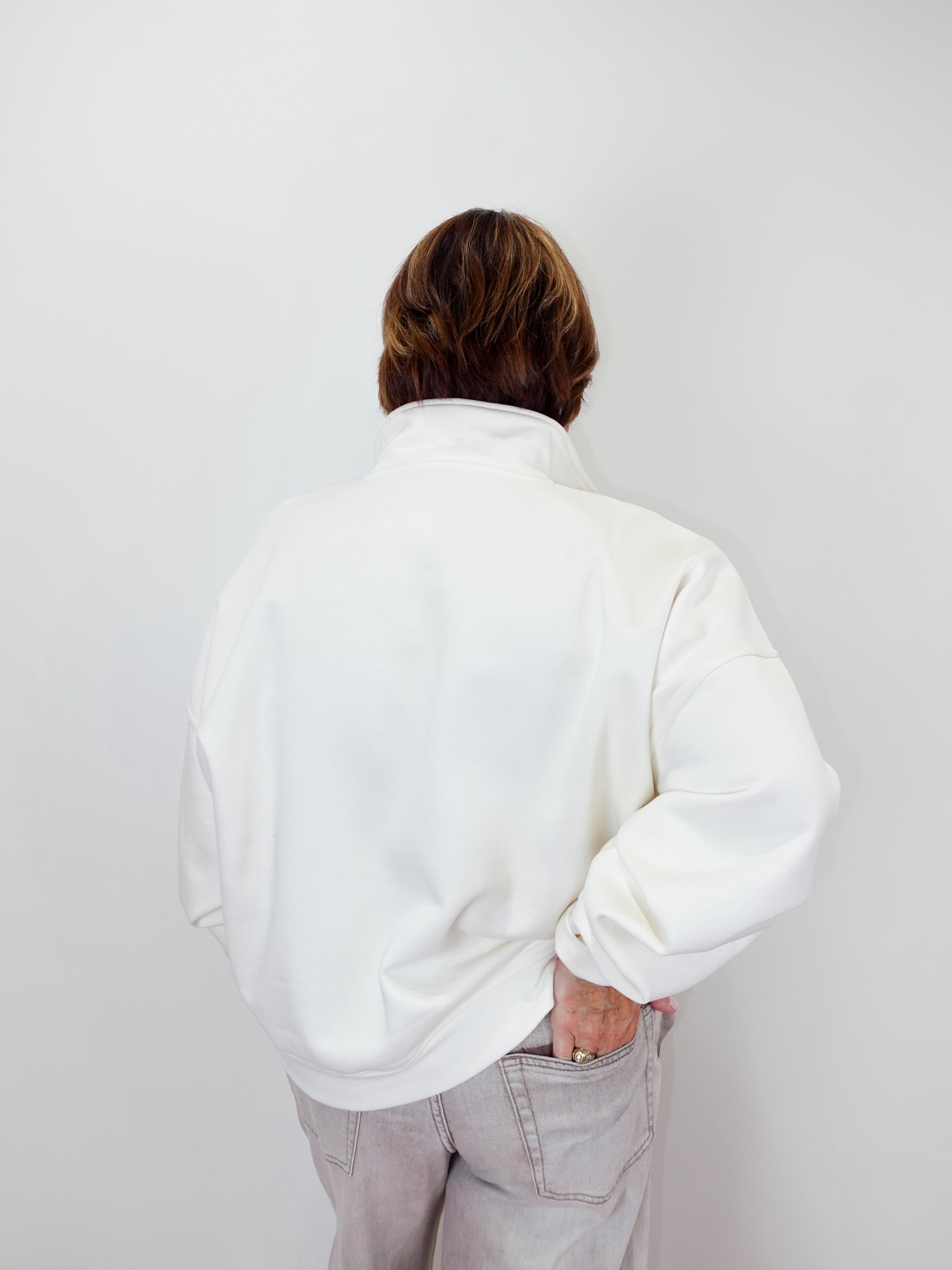 Person wearing a white sweatshirt and light gray pants against a plain background