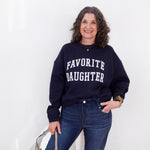 Woman wearing a navy sweatshirt with 'FAVORITE DAUGHTER' text, standing against a white background.
