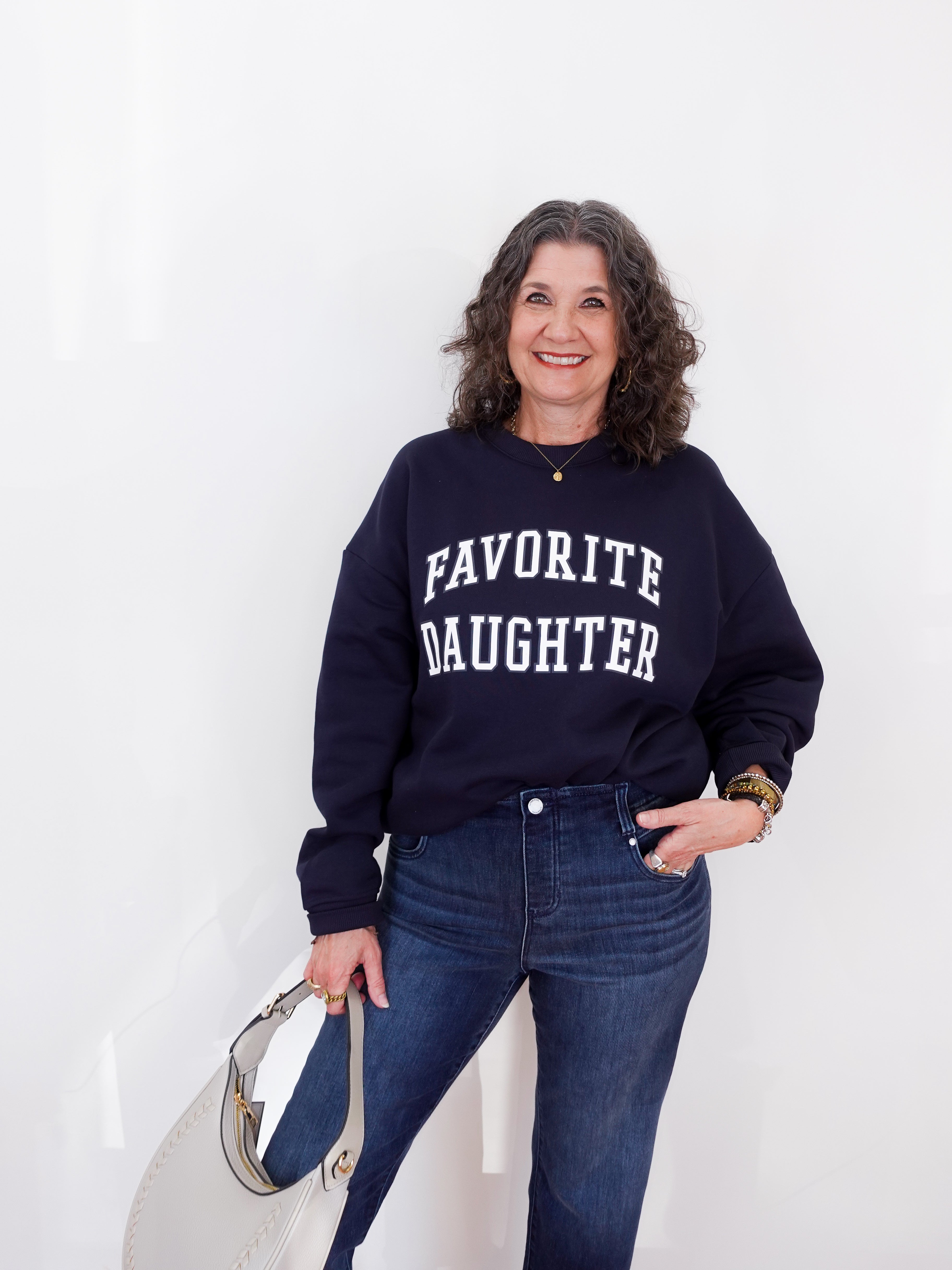 Woman wearing a navy sweatshirt with 'FAVORITE DAUGHTER' text, standing against a white background.