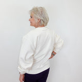 Person wearing a white sweatshirt and dark pants against a plain background