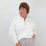 Person wearing a white sweater and light gray pants against a plain background