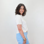 Woman wearing a white shirt and light blue skirt against a white wall.