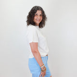 Woman wearing a white shirt and light blue skirt against a white wall.