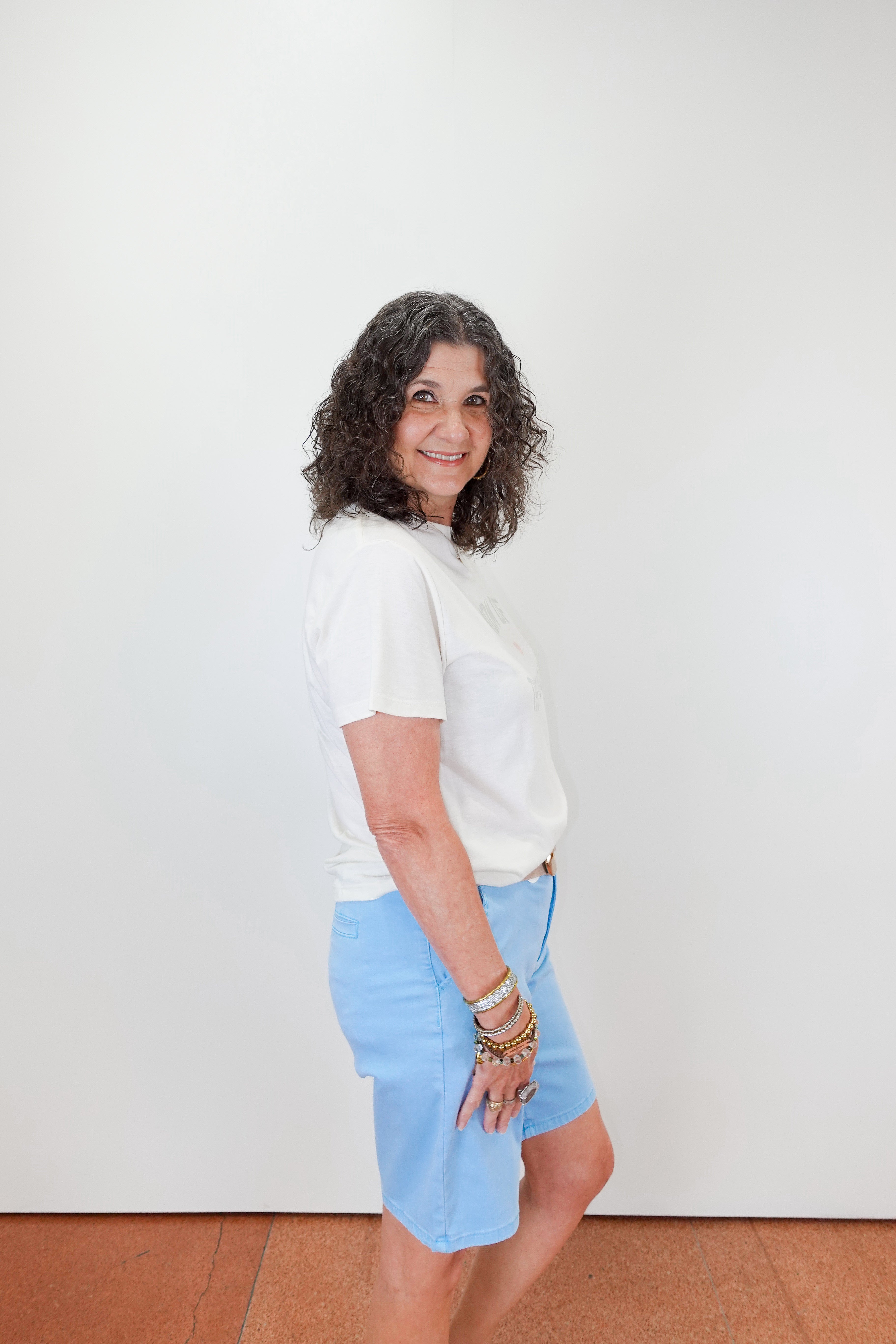 Woman wearing a white shirt and light blue skirt against a white wall.