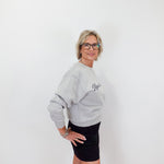 Woman wearing a gray sweatshirt with a logo and a black skirt on a white background