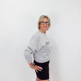 Woman wearing a gray sweatshirt with a logo and a black skirt on a white background