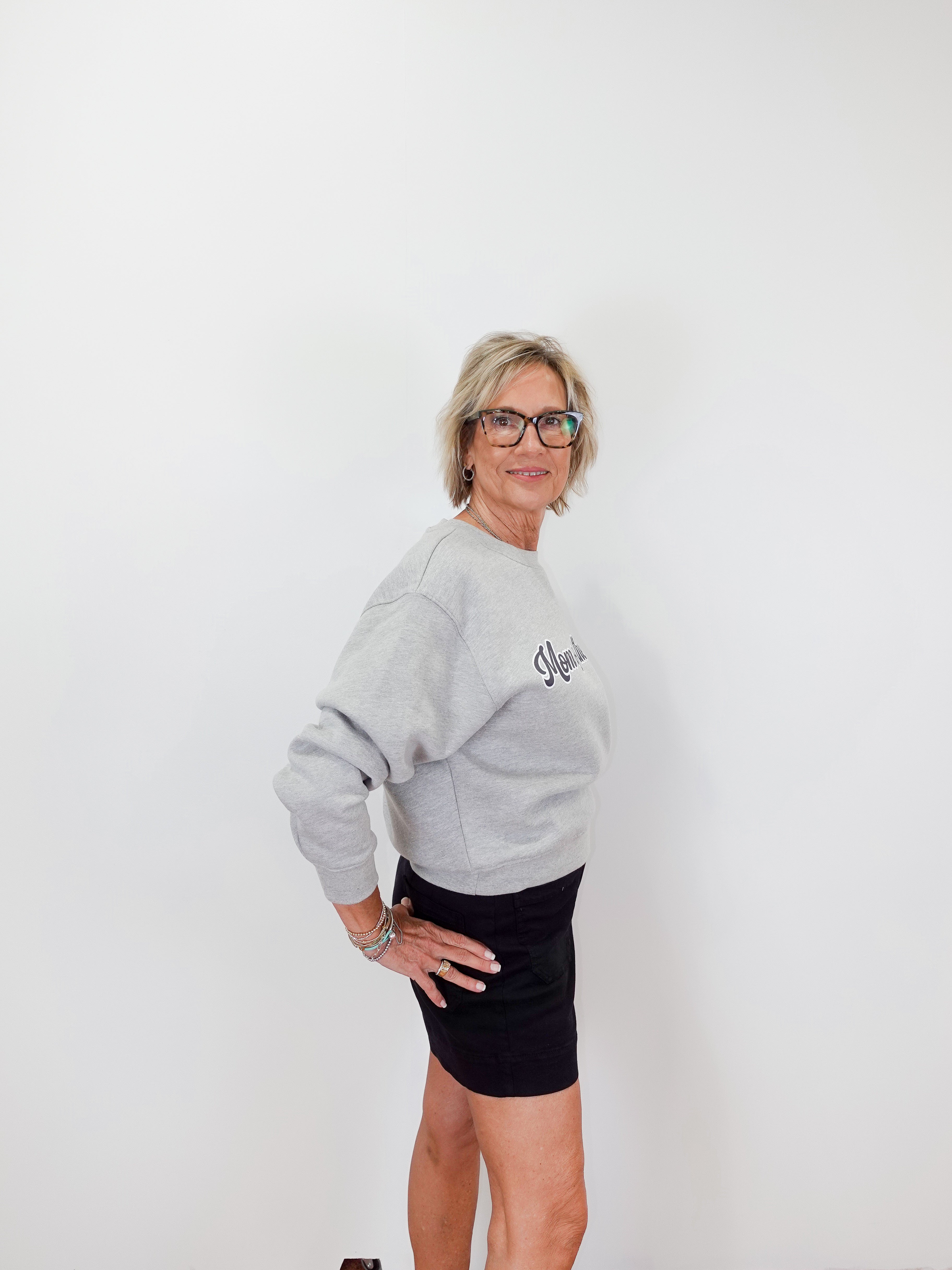 Woman wearing a gray sweatshirt with a logo and a black skirt on a white background