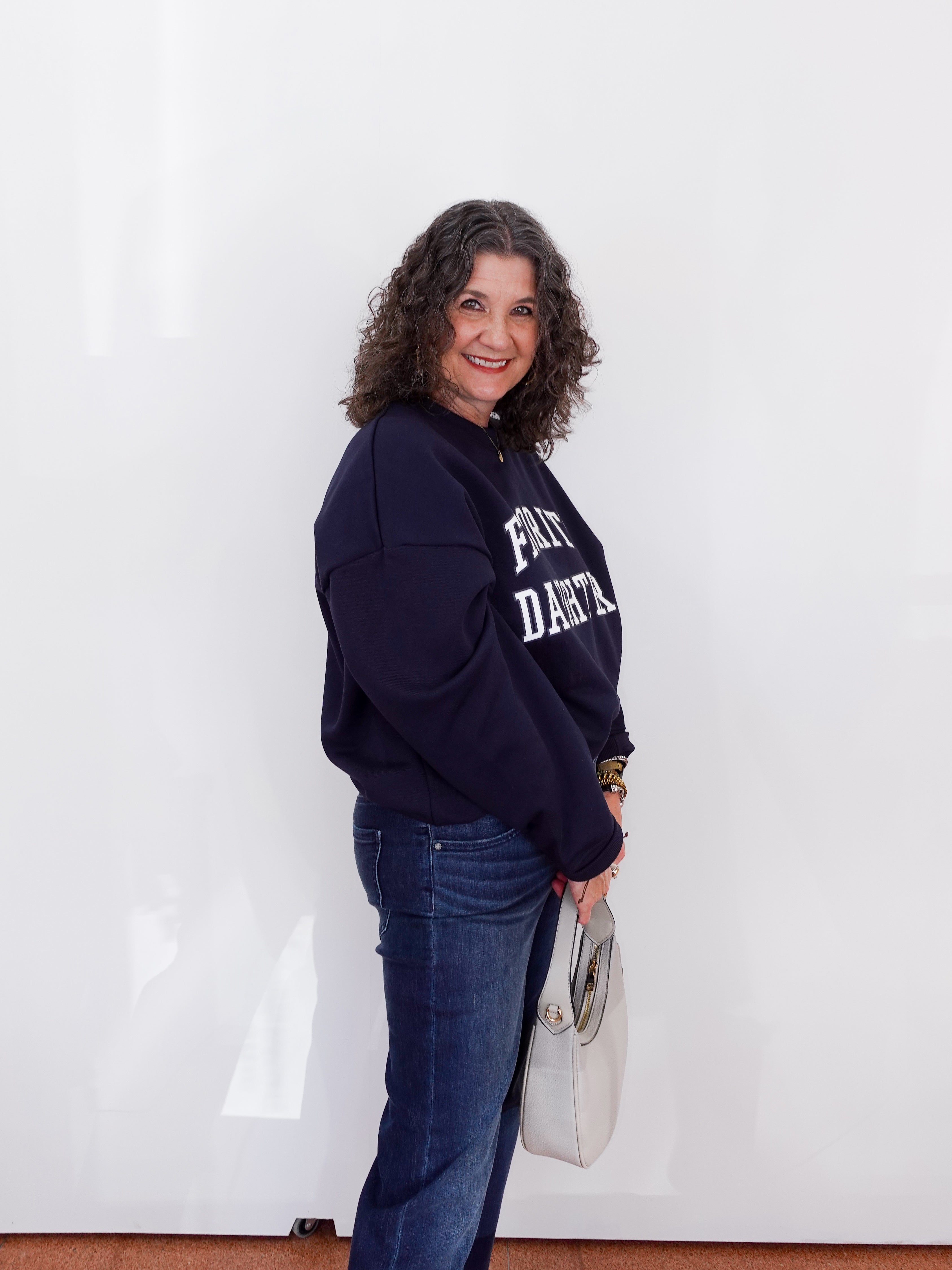 Woman wearing a navy blue sweatshirt with text, standing against a white wall.