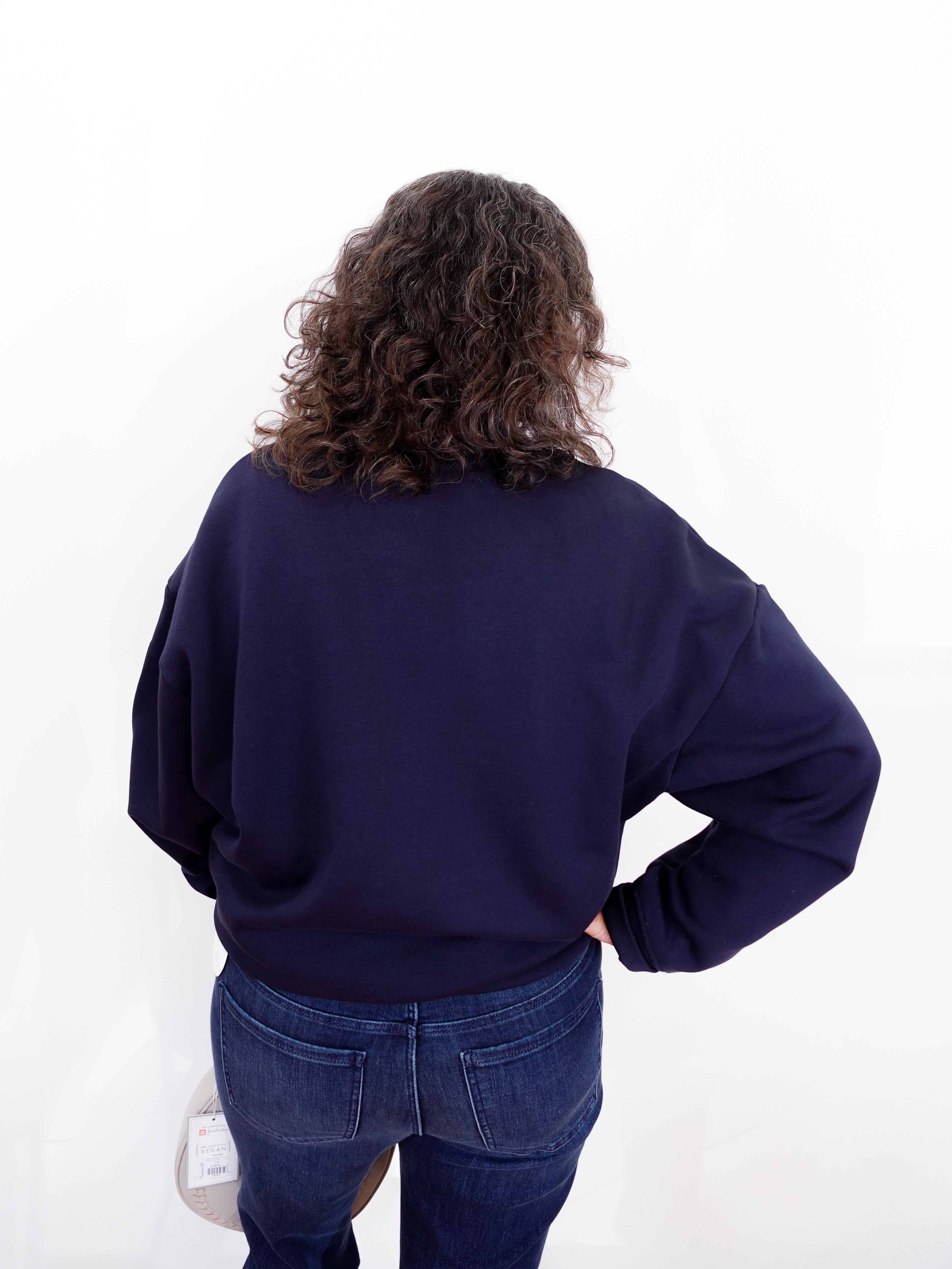 Person wearing a navy blue sweatshirt and jeans on a white background