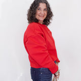 Woman wearing a red sweatshirt and blue jeans against a white background