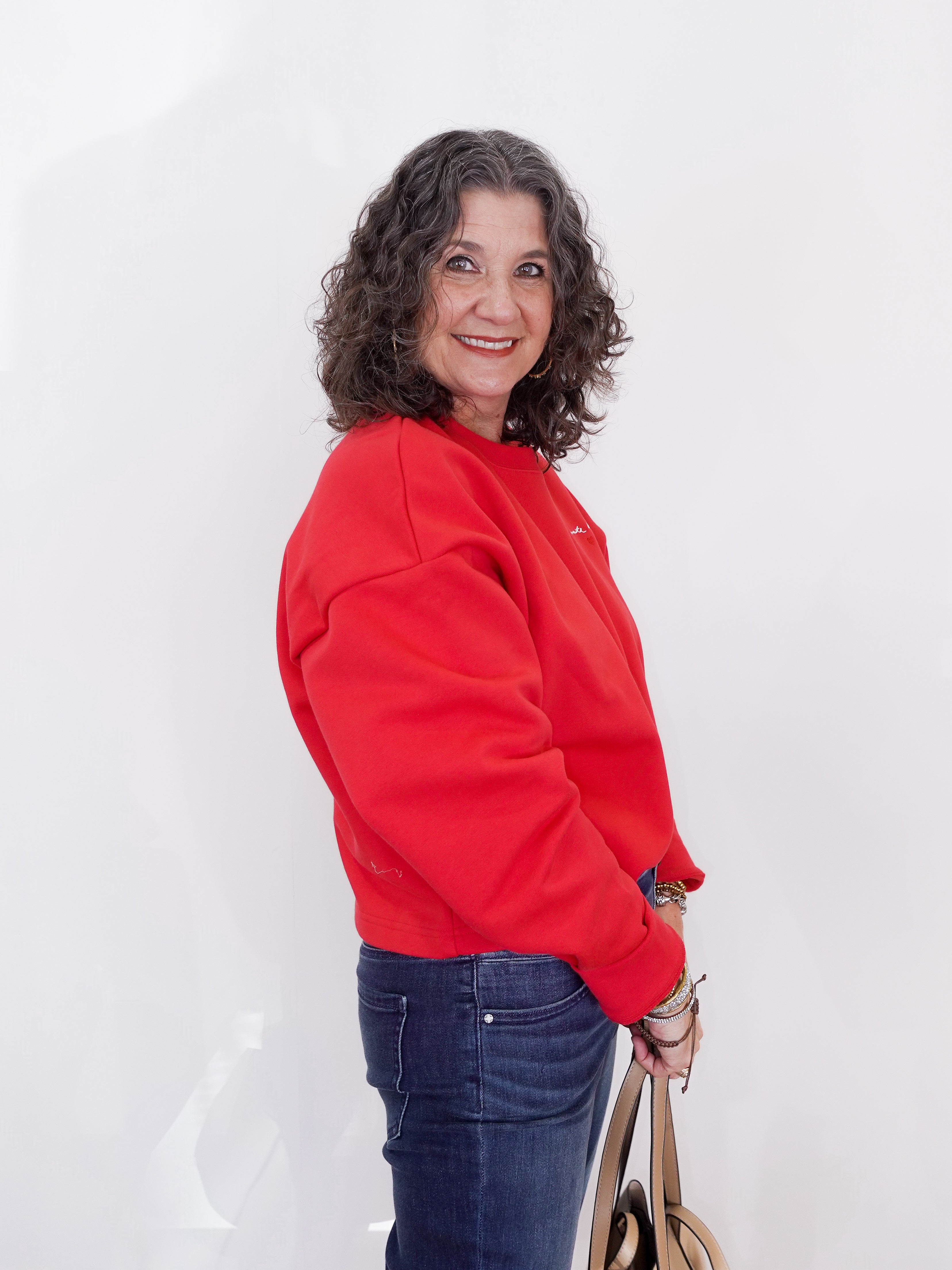 Woman wearing a red sweatshirt and blue jeans against a white background