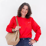 Woman wearing a red sweatshirt with text, holding a beige handbag against a white background
