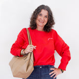Woman wearing a red sweatshirt with text, holding a beige handbag against a white background