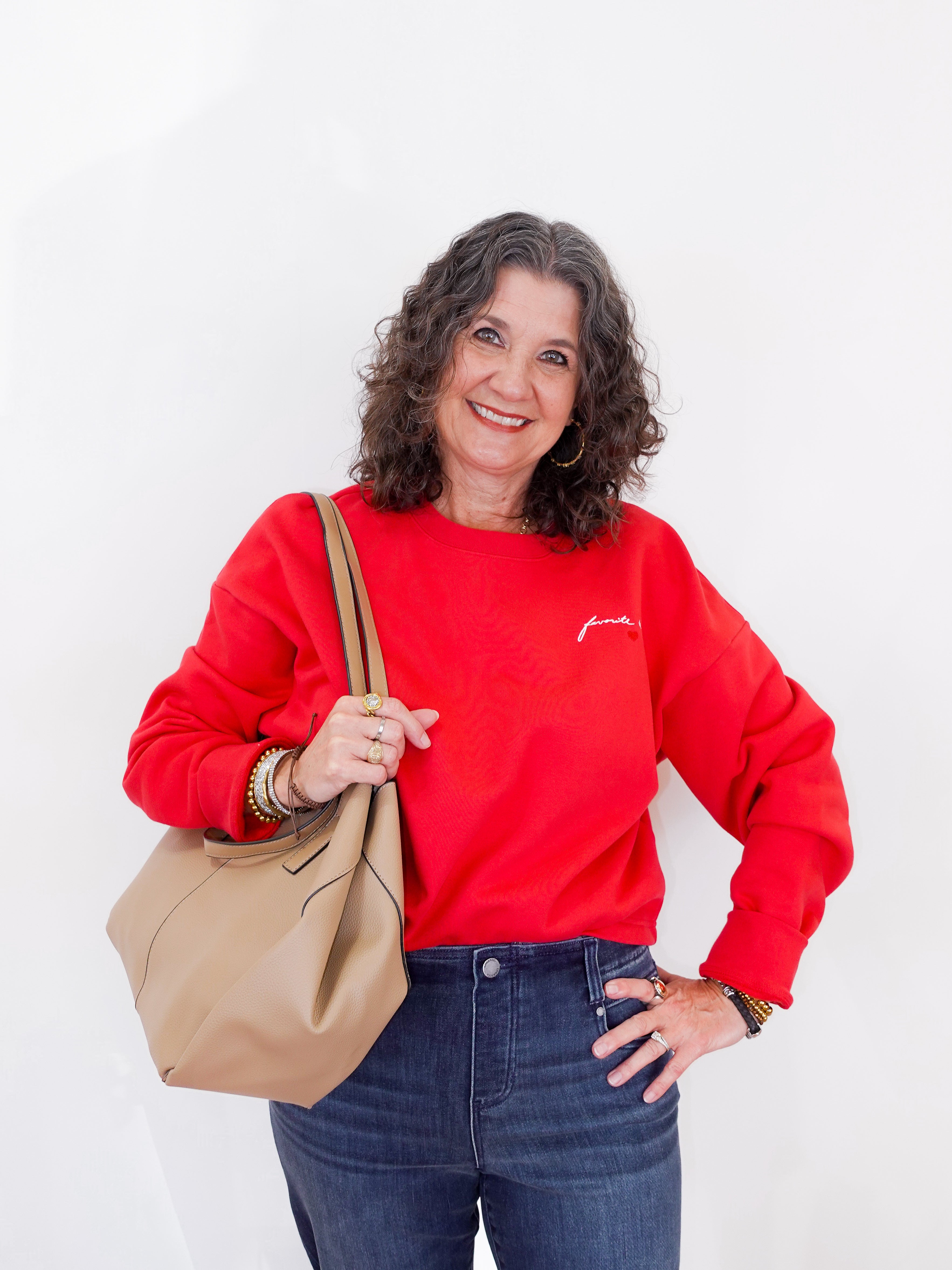 Woman wearing a red sweatshirt with text, holding a beige handbag against a white background