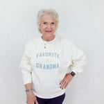 Woman wearing a white sweatshirt with 'Favorite Grandma' text on a plain background