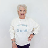Woman wearing a white sweatshirt with 'Favorite Grandma' text on a plain background